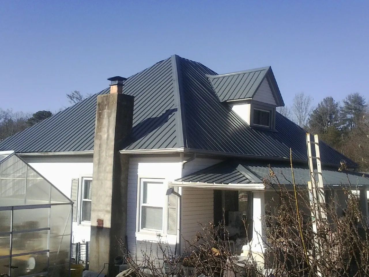 Dark blue standing seam metal roof on a white farmhouse with dormer — Slate & Tile Roof Repair by Roofing Brothers in Coffeyville