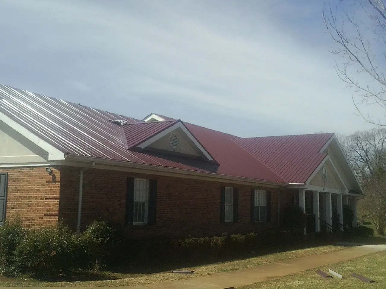 Red metal roof with gabled entries on a long brick building, from a Hail Damage Roof Repair job in Coffeyville