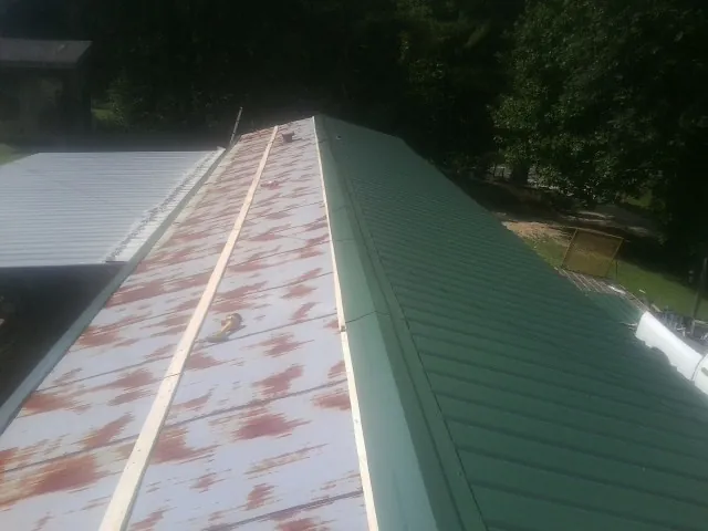 Old rusted panels beside newly installed green metal roofing — Wind Damage Roof Repair by Roofing Brothers in Coffeyville