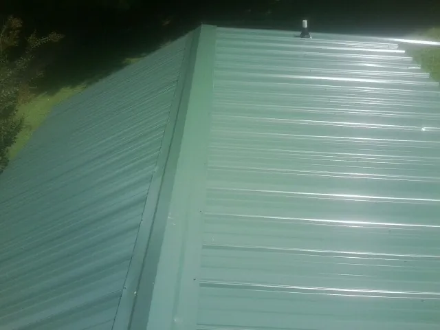 New green metal panels meeting at the ridge of a roof — Flat Roof Repair work by our crew in Coffeyville