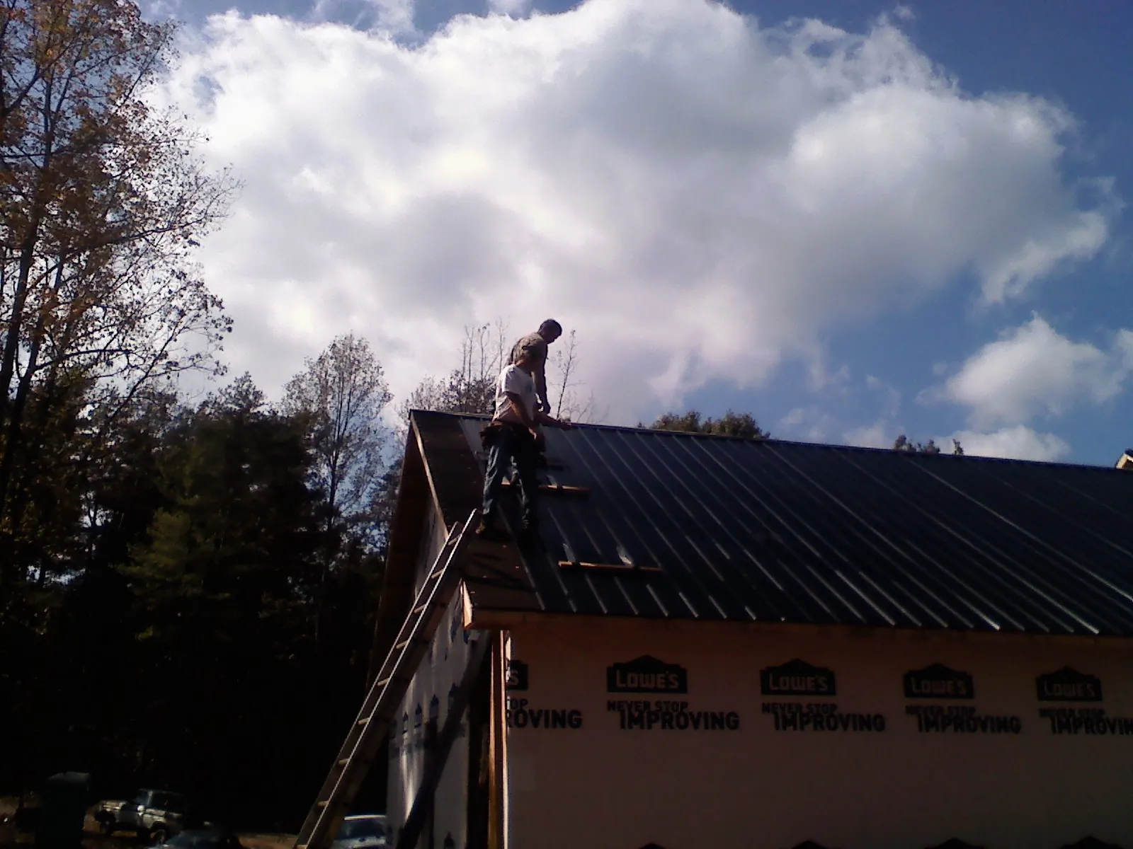 Roofer fastening dark metal panels high against a cloudy sky, from a Roof Inspection job in Coffeyville
