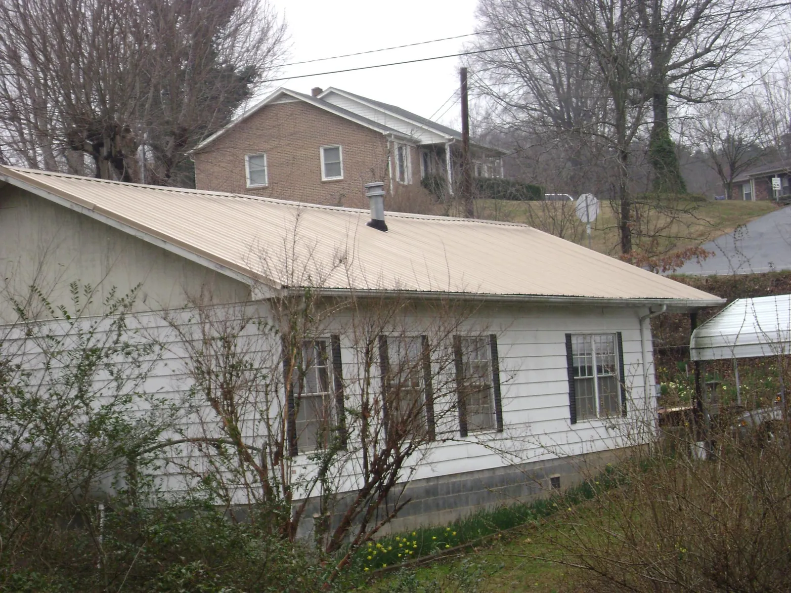 Tan metal roof on a white sided house set into a hillside — Commercial Roofing by Roofing Brothers in Coffeyville