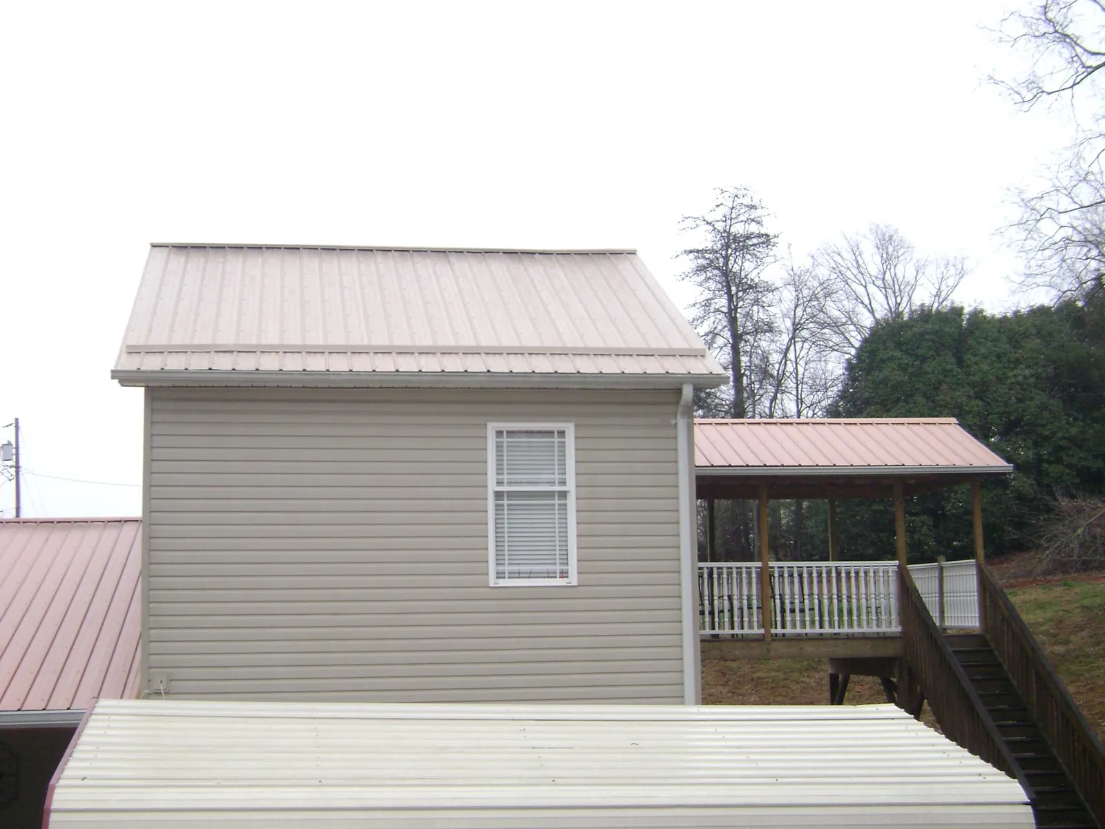 Tan metal roofs on a two story addition and attached porch, from a Roof Replacement job in Coffeyville