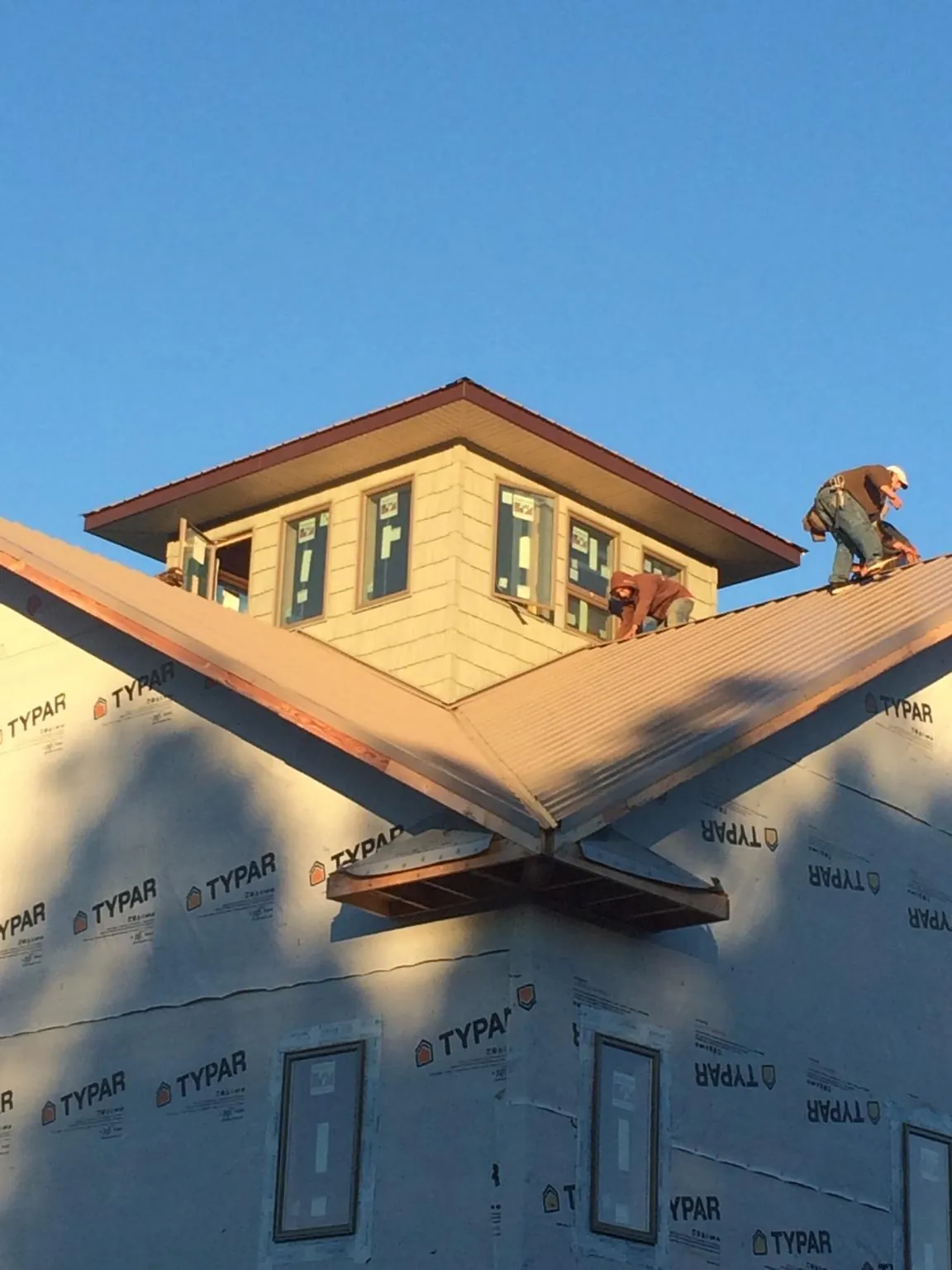 Roofers working around a rooftop cupola on a new metal roof at sunset — Roof Waterproofing in Coffeyville by Roofing Brothers